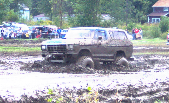 Mud-covered SUV stuck in a mud pit, with spectators in the background