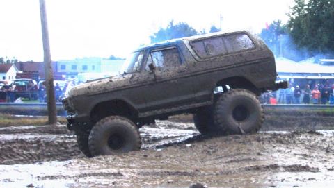 1979 Ford Bronco - A heavily muddied Ford Bronco navigates a challenging mud bog with large tires.