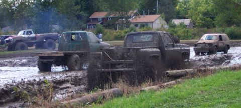 1979 Ford Bronco - Several trucks are navigating a muddy track, kicking up a lot of spray.