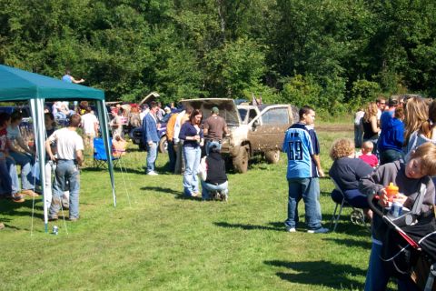 1979 Ford Bronco - A group of people gather around a muddy SUV with its hood up at an outdoor event.