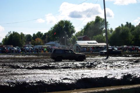 1979 Ford Bronco - An SUV navigates a muddy course during an event with onlookers present.