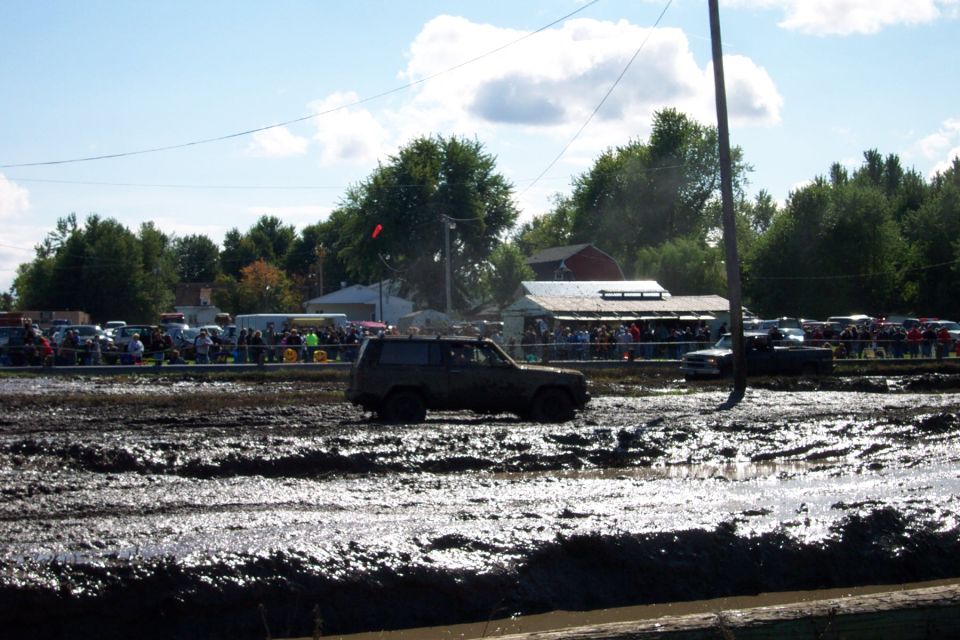 Dark colored SUV driving through a muddy track with spectators in the background
