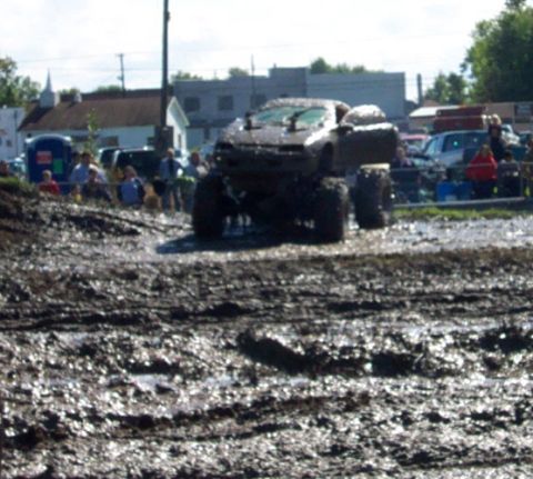 1979 Ford Bronco - A heavily modified truck navigates a muddy track with spectators observing the event.