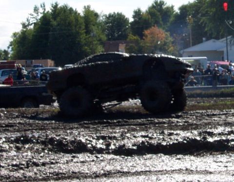 1979 Ford Bronco - A heavily mud-caked vehicle navigates a challenging off-road course with onlookers watching.