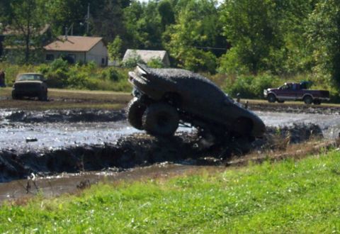 1979 Ford Bronco - An SUV is stuck deep in a mud pit during a bogging event, with other vehicles visible in the background.
