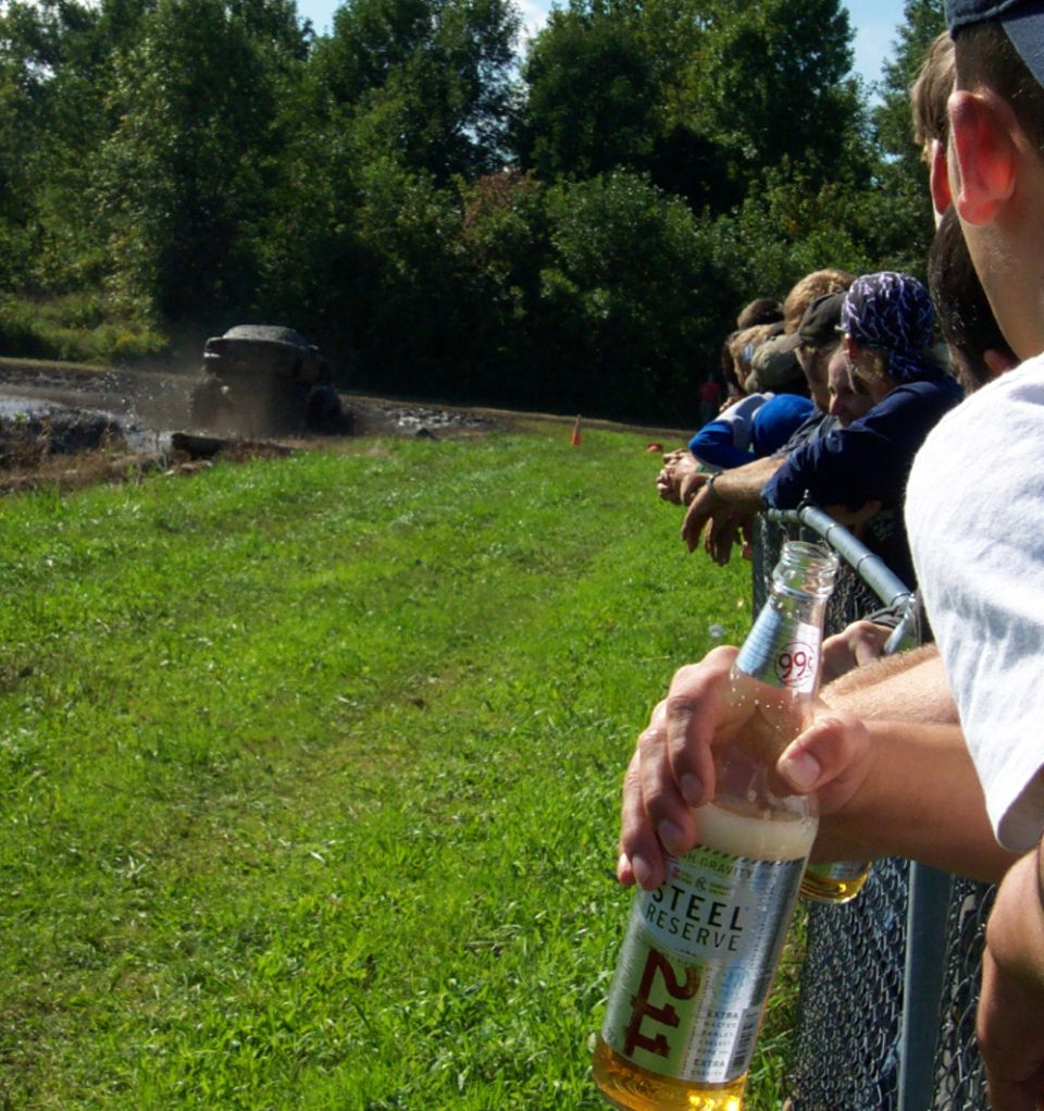 Off-road vehicle splashing through mud pit with spectators watching