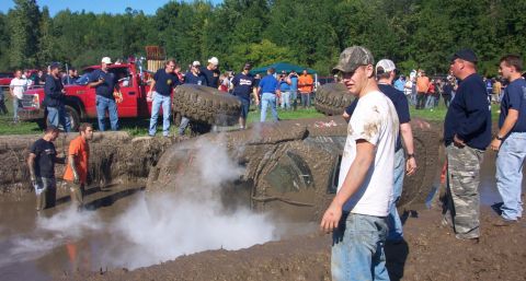 1979 Ford Bronco - A vehicle is stuck and overturned in a mud pit during an off-road event, with spectators watching.
