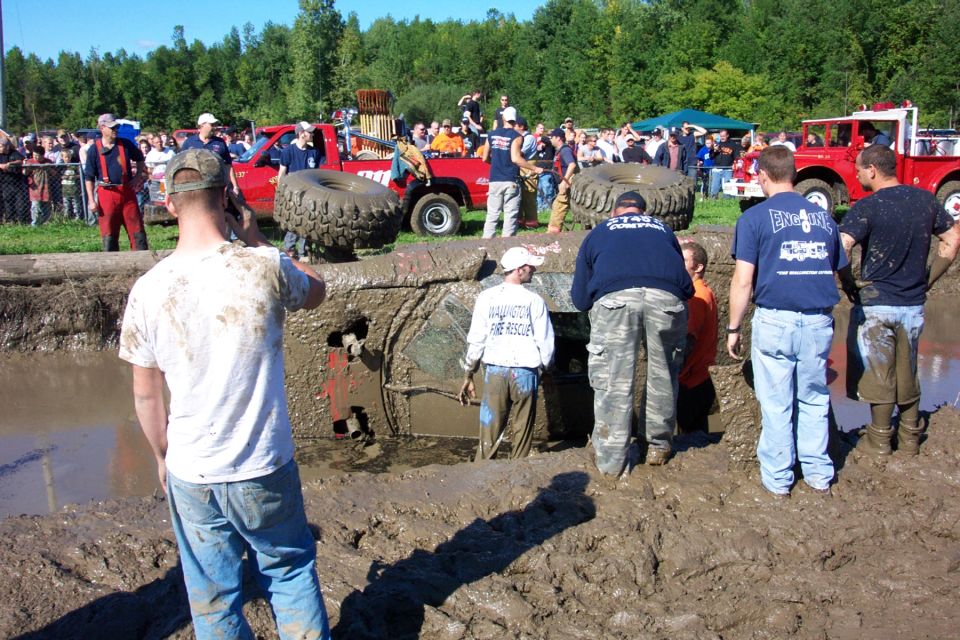 Mud bog event with a vehicle stuck deep in the muck and spectators around