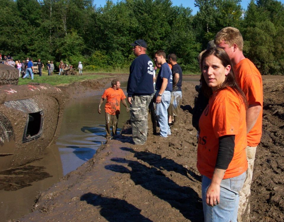 Mud-covered vehicle stuck in a mud pit with onlookers
