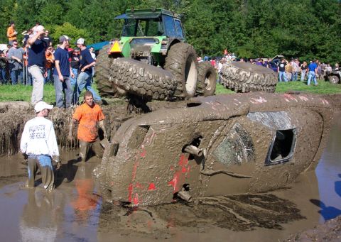 1979 Ford Bronco - A tractor is positioned precariously over a vehicle stuck deep in the mud during an event.