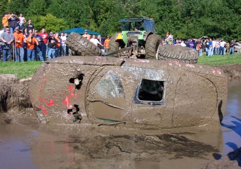 1979 Ford Bronco - A vehicle is stuck on its side in the mud, with a tractor and onlookers present at a mud bog event.
