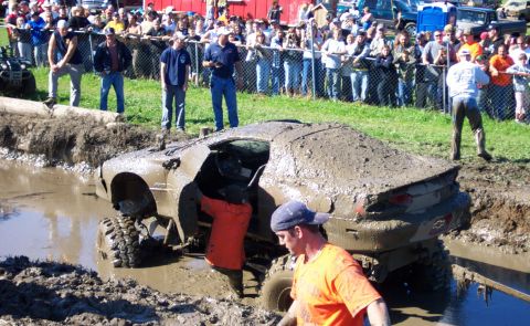 1979 Ford Bronco - A car is submerged in a mud pit during an event, with spectators gathered behind a fence.