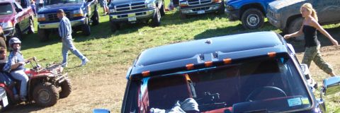 1979 Ford Bronco - A dark truck's interior and roof are visible, with several other vehicles and people in the background.