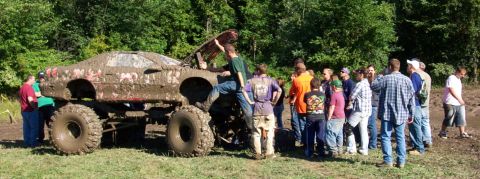 1979 Ford Bronco - A group of people observe a heavily modified, mud-covered truck in an outdoor setting.