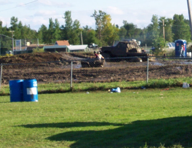 Mud bogging event with a modified truck and a portable toilet in the background