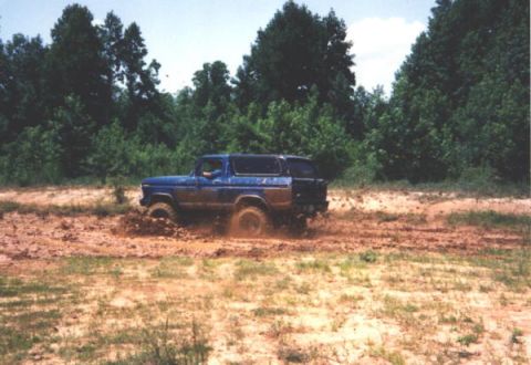 1999 Ford Crown Victoria - Blue Ford Bronco navigating a muddy off-road trail.