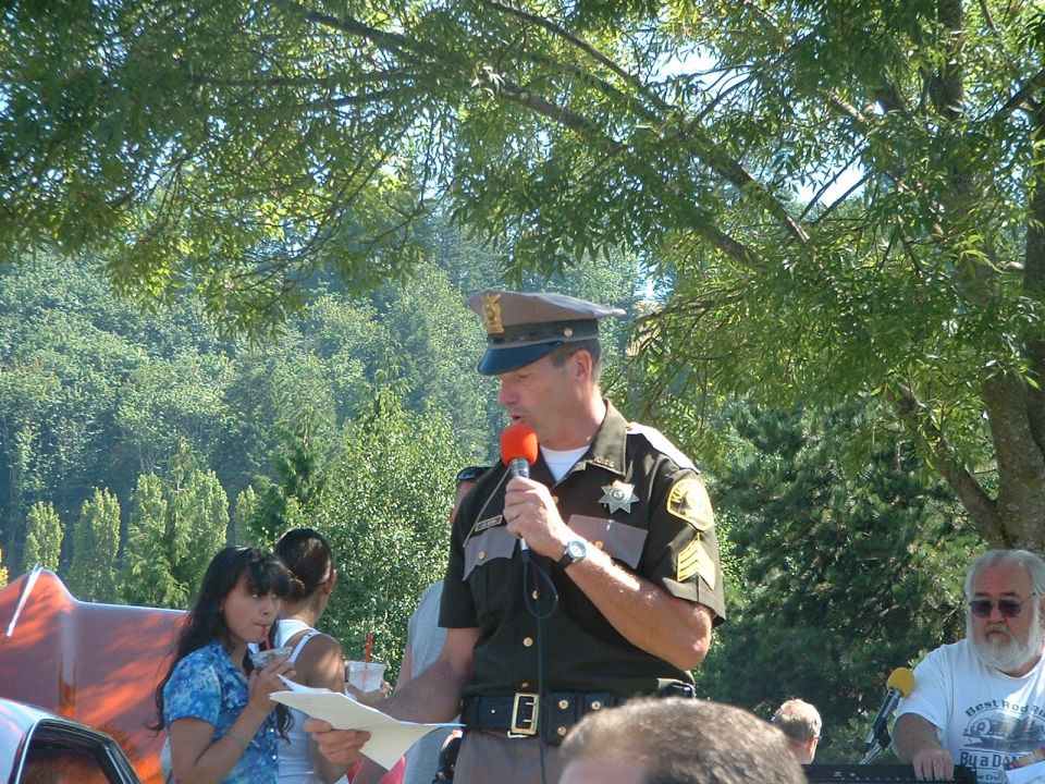 Sheriff speaking into a microphone at an outdoor event with people around