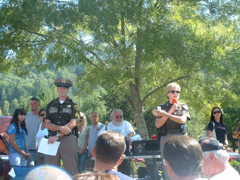 2000 Ford Crown Victoria - Two police officers address a gathering outdoors under a large tree.