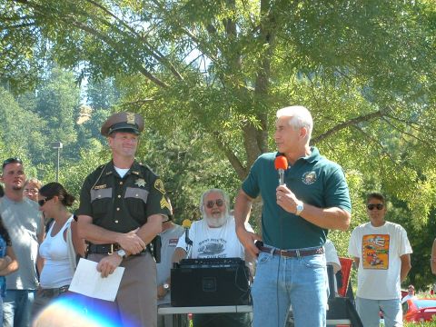 2000 Ford Crown Victoria - Outdoor event with a sheriff and a speaker addressing a crowd under trees.