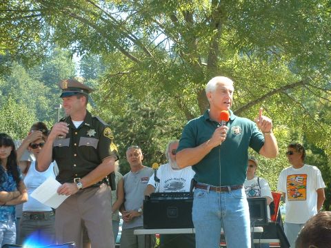 2000 Ford Crown Victoria - A man in a sheriff's uniform stands with papers while another man speaks into a microphone at an outdoor event.
