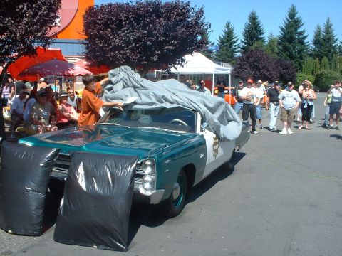 2000 Ford Crown Victoria - A 1967 Plymouth Fury I police car is partially uncovered at an outdoor event.