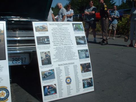 2000 Ford Crown Victoria - A display board lists sponsors and individuals at an outdoor event, with a car's license plate in the foreground.