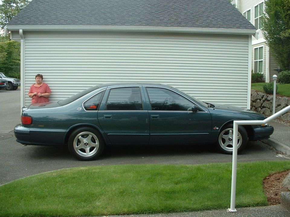 Green 1996 Chevrolet Impala SS sedan parked on asphalt next to a light-colored garage