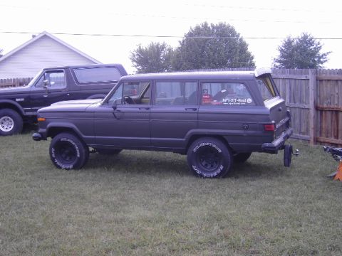 1977 Jeep Wagoneer - A dark gray 1977 Jeep Wagoneer is parked on a grassy lawn next to a dark SUV.