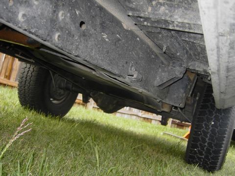 1977 Jeep Wagoneer - A close-up view of the undercarriage of a vehicle, showing the frame, suspension, and tires on a grassy lawn.