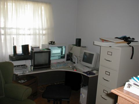 1999 Ford Crown Victoria - A cluttered office space features a corner desk with several computer monitors and peripherals, alongside a filing cabinet.