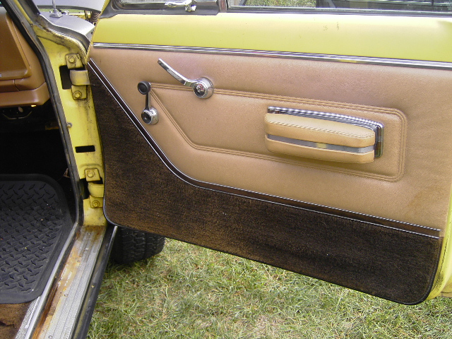 Yellow Jeep Wagoneer interior door panel with tan upholstery, chrome handle, and dark textured lower section. Visible door jamb and floor mat