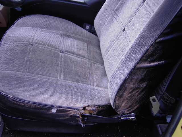 Close-up of a torn car seat with visible damage to the upholstery and foam