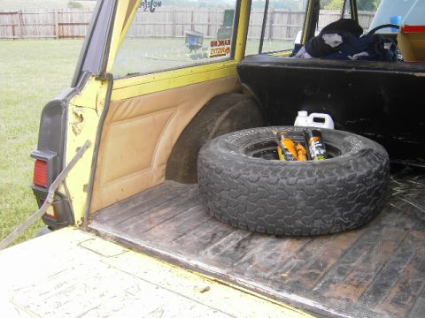 1977 Jeep Wagoneer - The cargo area of a yellow 1977 Jeep Wagoneer contains a spare tire, bottles of fluid, and spray cans.
