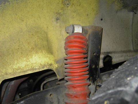 1977 Jeep Wagoneer - Close-up view of a red shock absorber and yellow fender well, showing suspension parts.