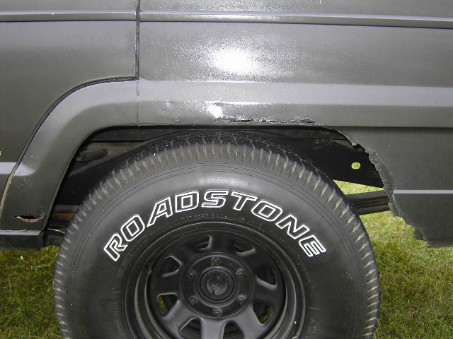 1977 Jeep Wagoneer rear wheel well showing rust and a ROADSTONE tire