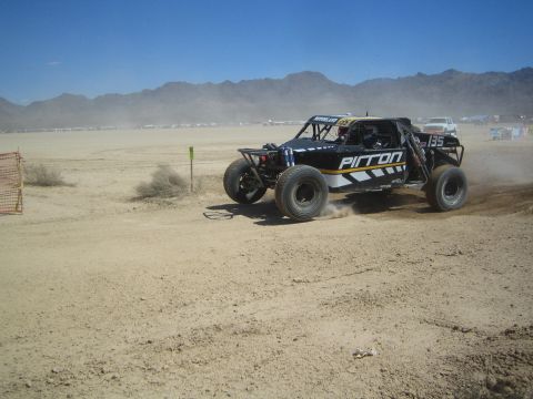 1990 Ford Bronco - black off-road race buggy with Pirron lettering races across a dusty desert flat below distant mountains.
