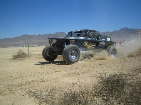 1990 Ford Bronco - black off-road race buggy with Corona Extra livery and number 37 powers across a dusty desert race course.