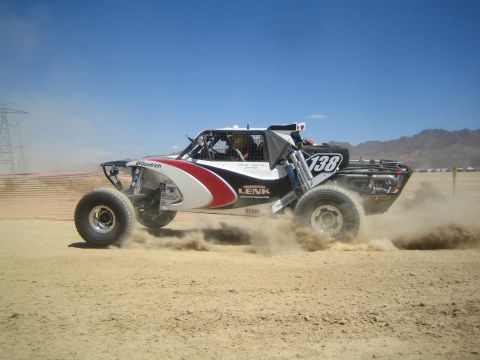 1990 Ford Bronco - white and red off-road race buggy marked number 138 catches air and throws dust on a desert race course.