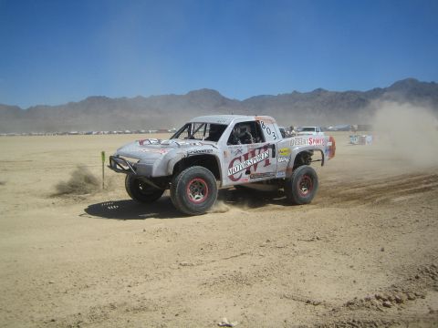 1990 Ford Bronco - silver and red off-road race truck marked number 803 slides through dirt on a dusty desert race course.