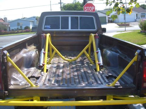 1985 Ford Ranger - Rear view of a brown pickup truck bed modified with a yellow roll bar and shock absorbers.