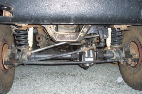 1994 Ford F-150 - The front axle and suspension system of a vehicle is shown from underneath, including the differential and shock absorbers.