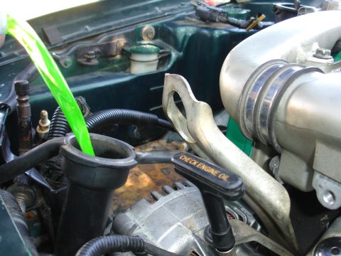 1993 Ford Taurus - Green fluid is poured into a vehicle's engine bay reservoir, with the "CHECK ENGINE OIL" dipstick visible in the foreground.