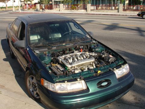 1993 Ford Taurus - 1993 Ford Taurus sedan with its hood open, revealing the V6 engine.