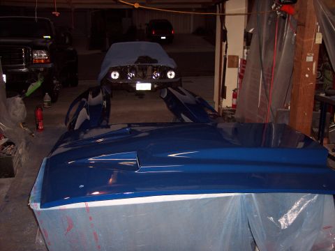 1971 Ford Mustang - Car parts, including a hood and fenders, are laid out in a garage next to a tarp-covered vehicle.