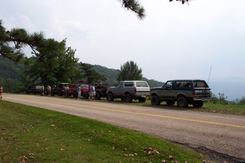 1987 Ford Bronco - A group of Ford Broncos are parked along a scenic highway overlook on a cloudy day.