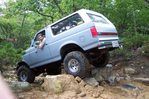 1987 Ford Bronco - A man drives a lifted 1987 Ford Bronco over a rocky trail.