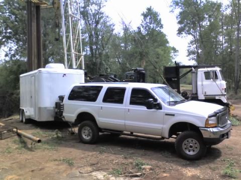 2000 Ford Excursion - A white 2000 Ford Excursion is seen towing a white trailer, with a drilling rig and another truck in the background.