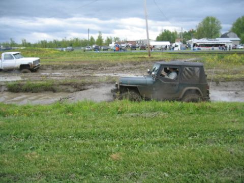 1978 Ford Bronco - A Jeep Wrangler navigates a muddy obstacle course, with a white pickup truck also visible in the mire.