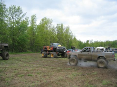 1978 Ford Bronco - Several modified trucks participate in a mud bogging event, with one pickup truck in the foreground kicking up dirt.