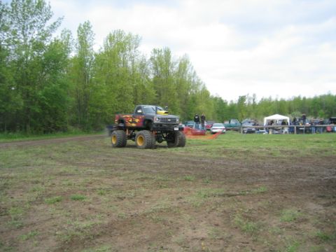 1978 Ford Bronco - A modified monster truck with flame decals is seen in an outdoor event area with spectators and other vehicles.